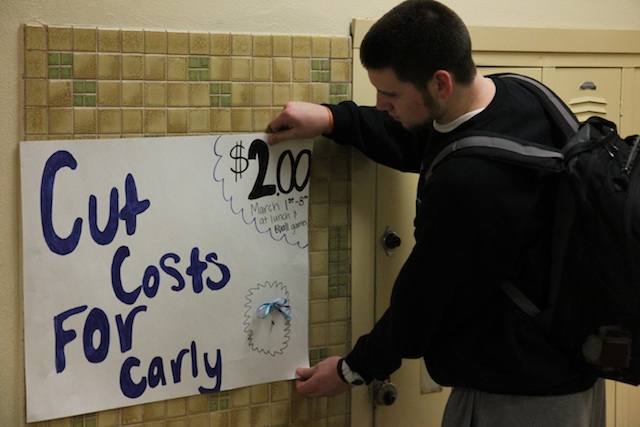 Senior Charlie Koch hangs a sign advertising the Cut Costs for Carly fundraiser, featuring a blue ribbon