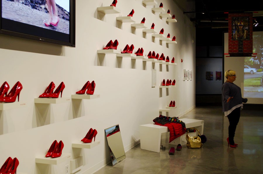 Red shoes line a wall within the exhibit. There are various signs placed nearby encouraging those at the exhibit to try them on.