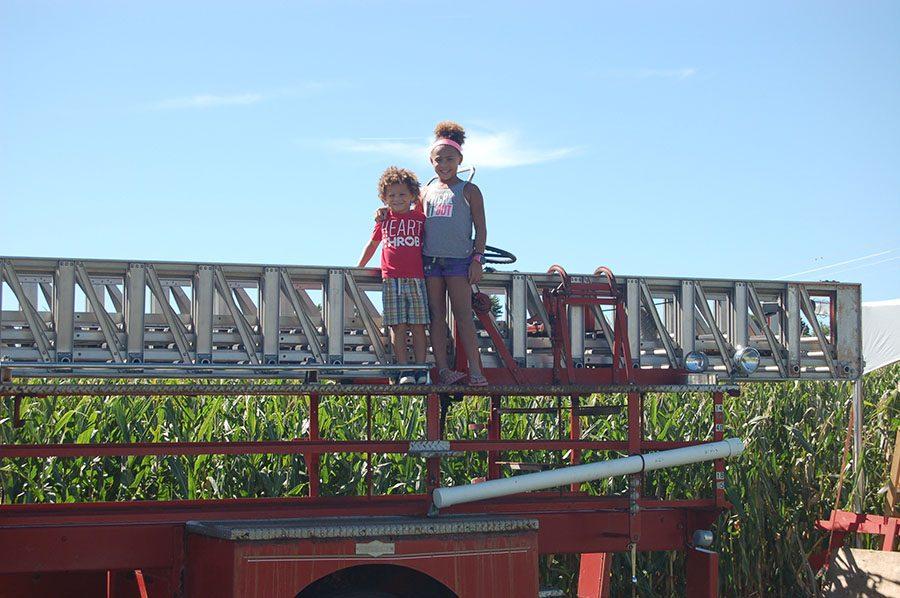Two children stand on top of a firetruck in front of the Severs Corn Maze. Tractors and other farm equipment were available to climb on.