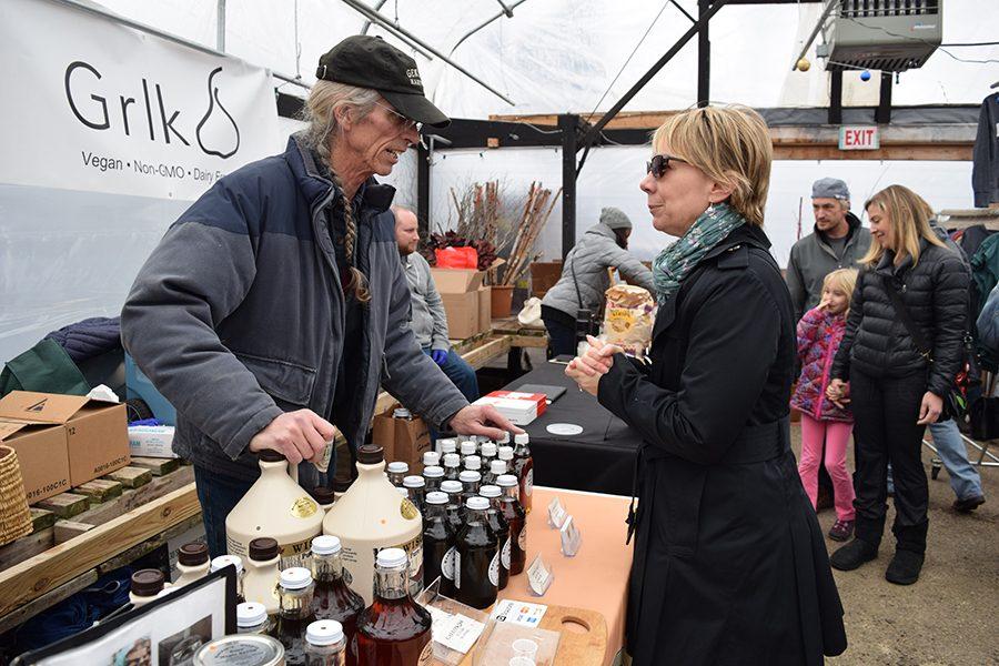 Susan Anderson talks to a vendor about types of syrup for sale at the market. The syrup comes in different sizes and flavors.