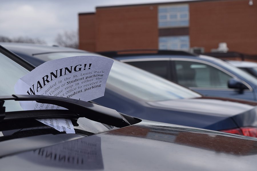 A parking violation warning lies under a cars windshield wipers in the student parking lot.