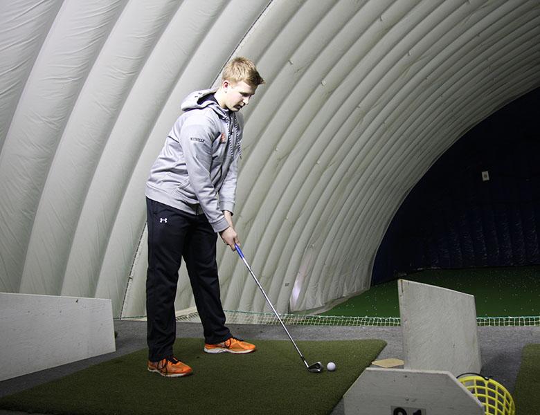 Junior captain Billy Nicholls practices with the golf team after school at the Brooklyn Park golf dome. The teams first varsity conference match will be held on April 10.