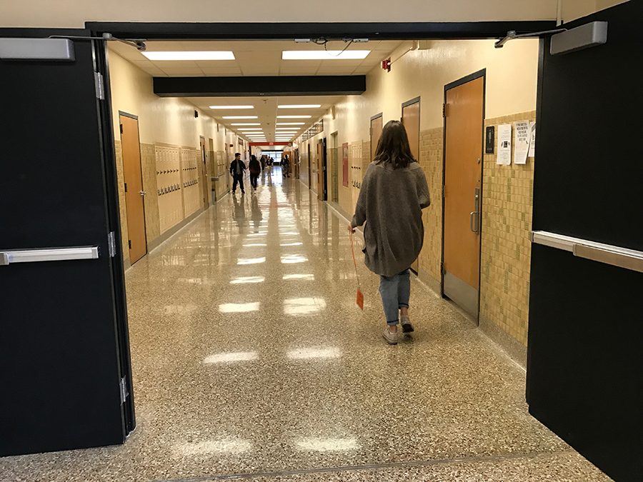 A student walks in a hallway during the class period. She holds a restroom pass to ensure she will not be penalized for walking without a pass.