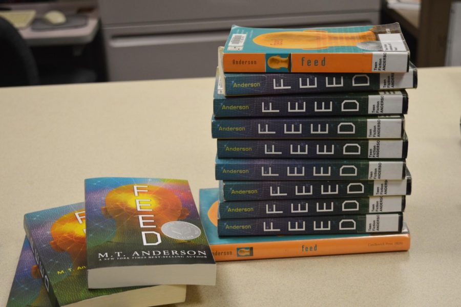 Copies of the book clubs new book, Feed, sit in the library waiting to be checked out. Feed is a dystopian novel about issues like corporate power and consumerism.
