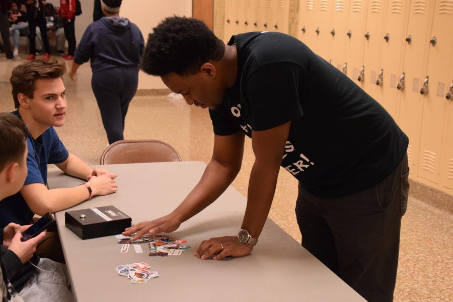Higher Achievement Program advisor Chris Weaver examines the stickers made by students in the Business Innovations class. Stickers can be made with any photo or design and are sold for 50 cents in the hallway outside of the lunchroom.