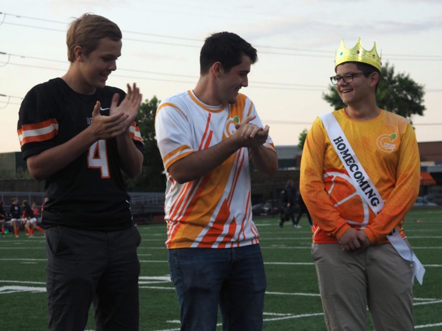 Homecoming king candidates Adam Bauer and Aidan Henry applaud Homecoming king Danny Hunegs during coronation Sept. 17 at the football stadium.