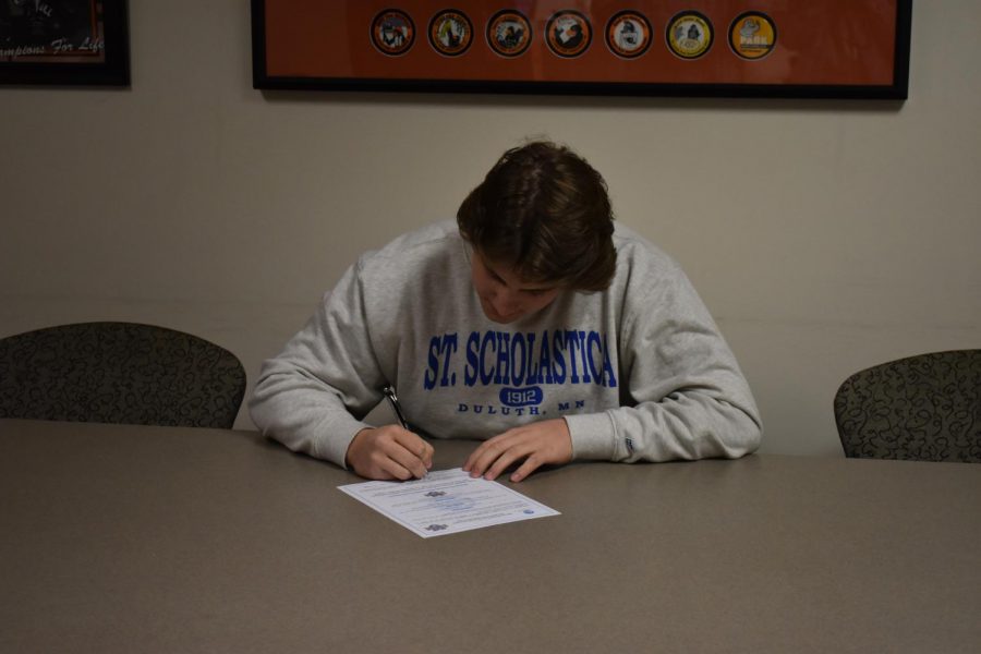 Senior Luke Boyum signs his commitment to the college of St. Scholastica in the athletic office. Boyum was accompanied by his coach, friends and family while he signed.