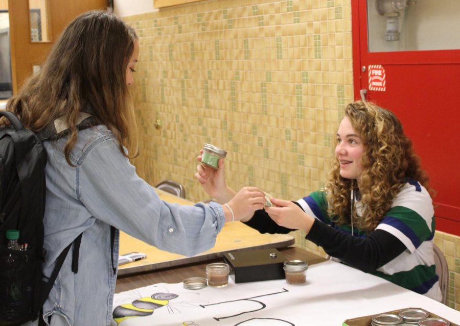 Sophomore Evie Gutzke sells a candle to sophomore Maia Seidel outside the lunch room Nov. 7. The candles are selling for seven dollars .