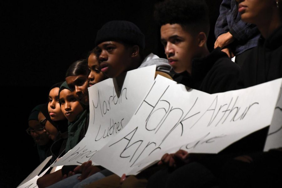 Student participants hold up signs of famous black individuals while other students speak during the introduction to the Black History Month presentation. 