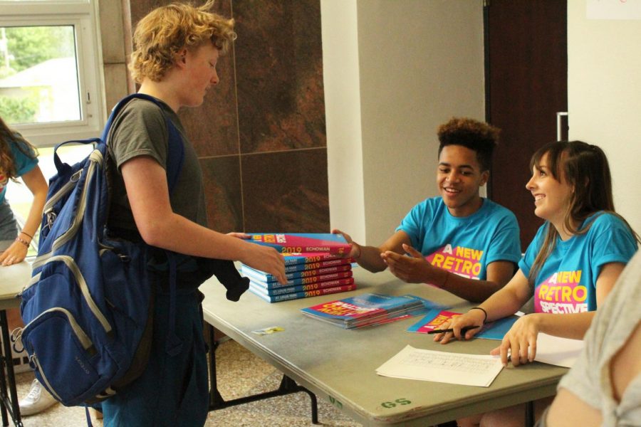 Sophomores Evan Nelson and Lauren Whiteman hand off a yearbook to sophomore Jasper Hoff May 29. Echowan distributed books May 29-30 during lunch. 
