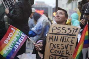 A protester waves a “love trumps hate” flag and holds a sign that reads, “Psst! MN Nice doesn’t cover: racism” at the anti-Trump protest Oct. 10 in front of Target Center.