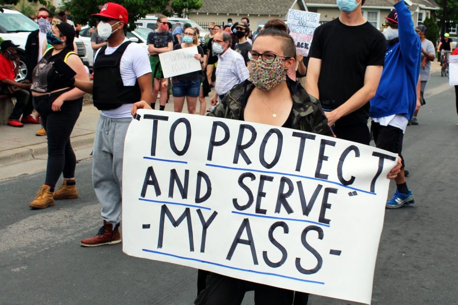 A woman holds a sign with the words “‘To protect and serve’ my ass” during a protest on Chicago Avenue to honor George Floyd May 25. After protests turned violent, many cities and counties have implemented mandatory curfews.