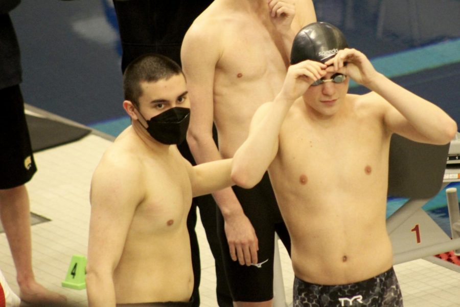 Senior Hiro McKee helps Andre Barajas put his swim cap on before swimming the 500 yard freestyle March 5. The team ended the season off strong with 11th and 8th places. 