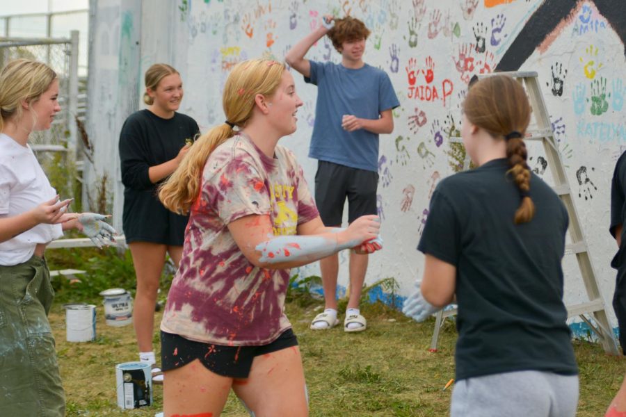 Senior Lily Olson gets ready to splatter paint on her fellow classmates. Seniors painting the wall has been going on for many decades.