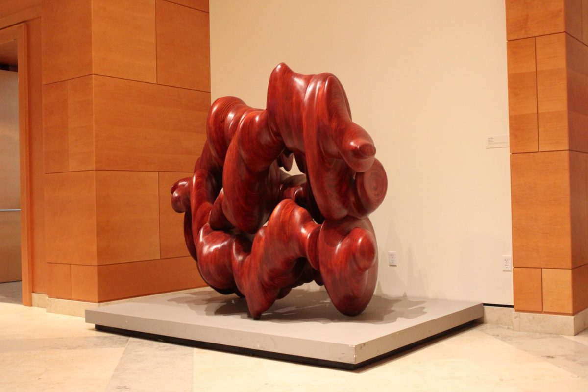 A varnished wooden sculpture stained to appear red presented on a platform at the Minneapolis Institute of Art. 