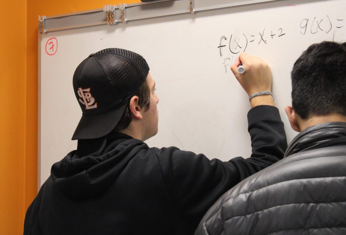 Juniors Ari Rose and Lorenzo Romero-Torres solve precalculus problems on the whiteboard Friday Dec. 1. Precalculus classes are exclusively AP this year, so students must take the higher-level class.
