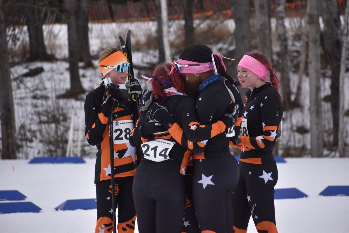 Pursuit skiers, eighth grader Adeline Stewart, seniors Jersey Miller, Ayelel Meyen, and Hanna Wilsey and junior Eleanor Lindeman, embrace and shed some tears after the final pursuit race. For the senior skiers, it was their last high school race.