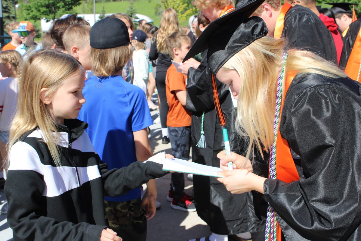Senior Avery Courneya signs young elementary schoolers year book as senior leave the bus to participate in the 2024 senior walk-through. The walk-through is an annual tradition where seniors can revisit their elementary schools to say goodbye.