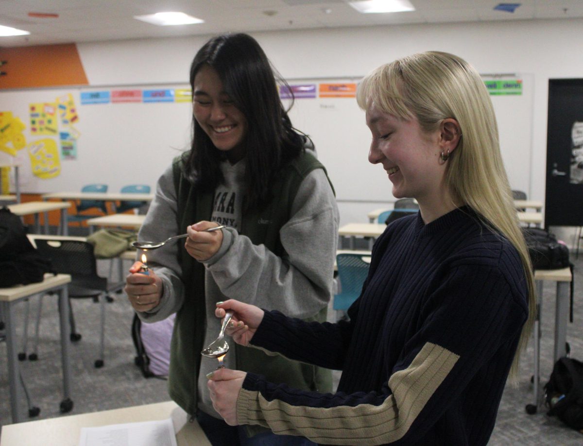 Junior club president Hannora Crouse and junior Tenzin Pedon melt wax on a spoon to pour into cold water Jan. 5. In German Club, members perform this old German tradition to predict how their year will go.