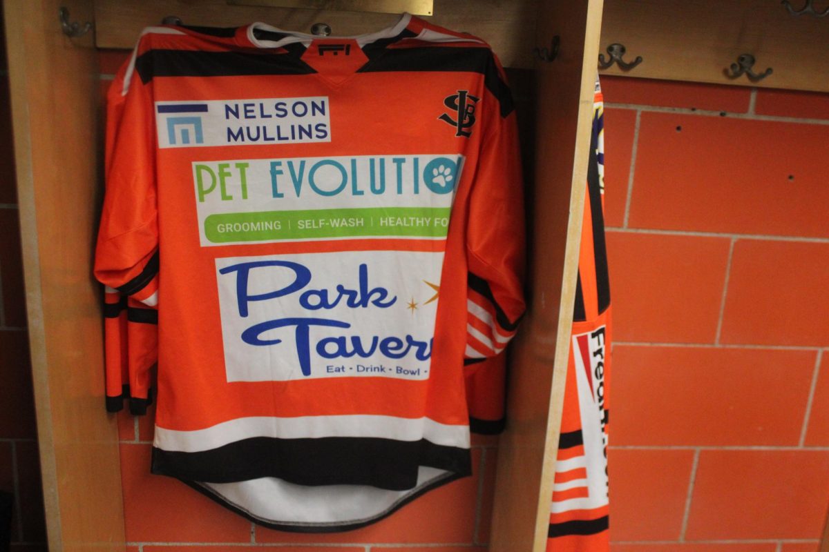 A boys hockey warm-up jersey hangs in a locker. Local businesses pay for their logo to be placed on these jerseys, helping fund transportation and equipment for the team.